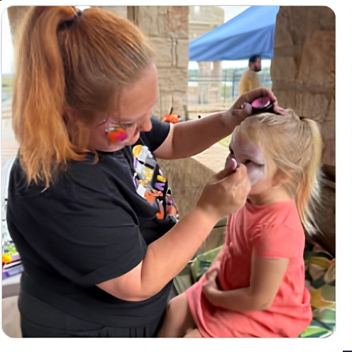 Sabrina painting a child's face outdoors
